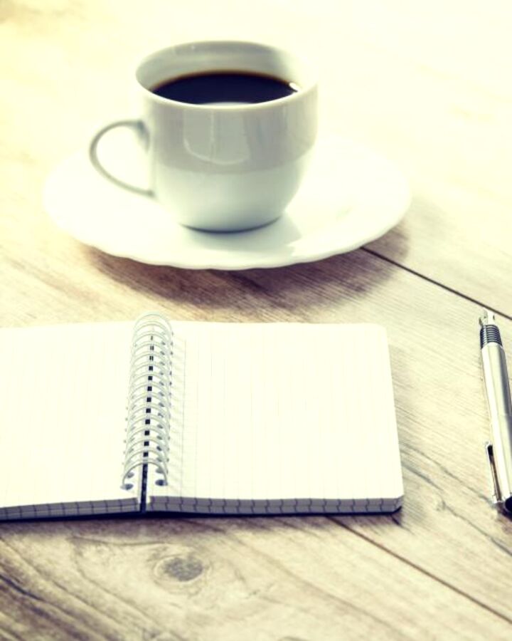 A notebook and coffee next to a laptop